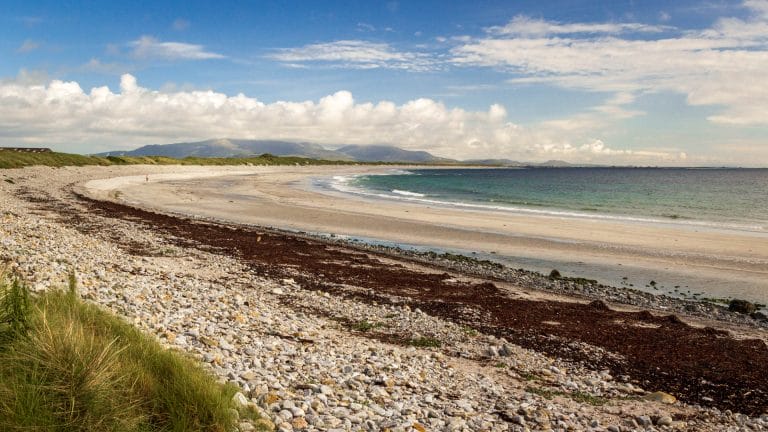 Ein sich biegender Strand mit Kiesel. Im Hintergrund ein Berg.