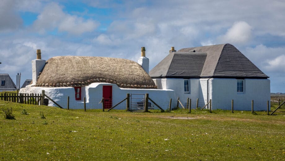 Ein weißes Haus mit einem Reetdach und einer roten Tür auf der Insel Tiree.