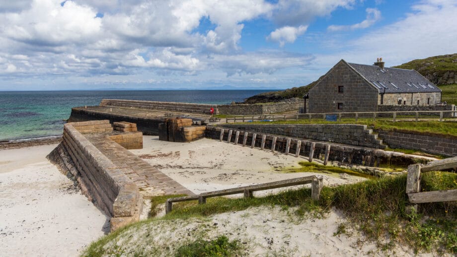 Ein kleines hafenbecken, das voller Sand ist und ein Haus dahinter auf Tiree bei Hynish.