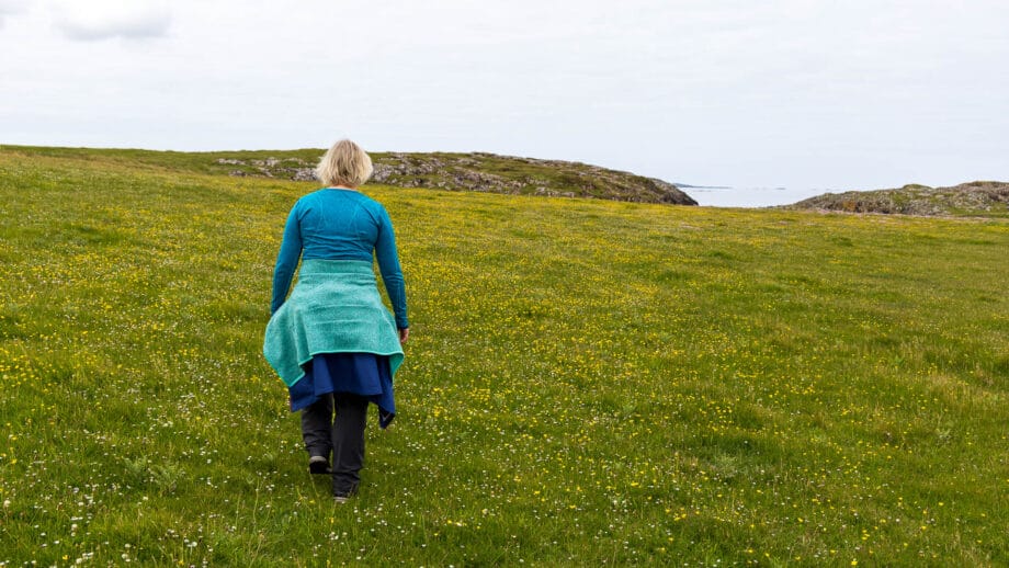 Eine Frau hat sich Jacken um die Hüfte gebunden und wandert durch eine Wiese