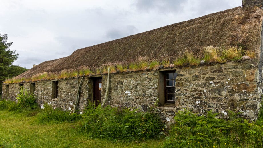 Ein reetgedecktes langes Steinhaus, umgeben von 