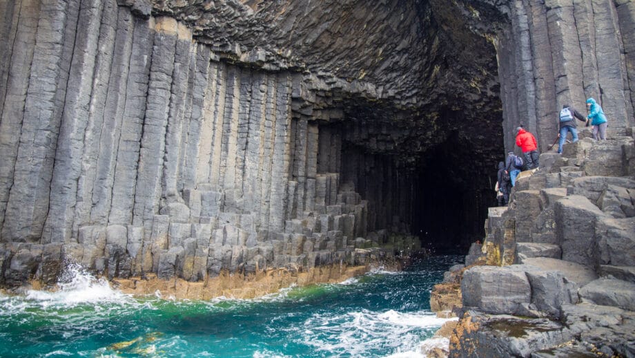 Eine Gruppe Menschen nähert sich der Fingals’s Cave auf Staffa. Sie besteht aus sechseckigen Basaltsäulen