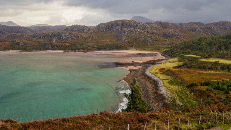 Eine Bucht mit einem Sandstrand darin und Bergen dahinter.